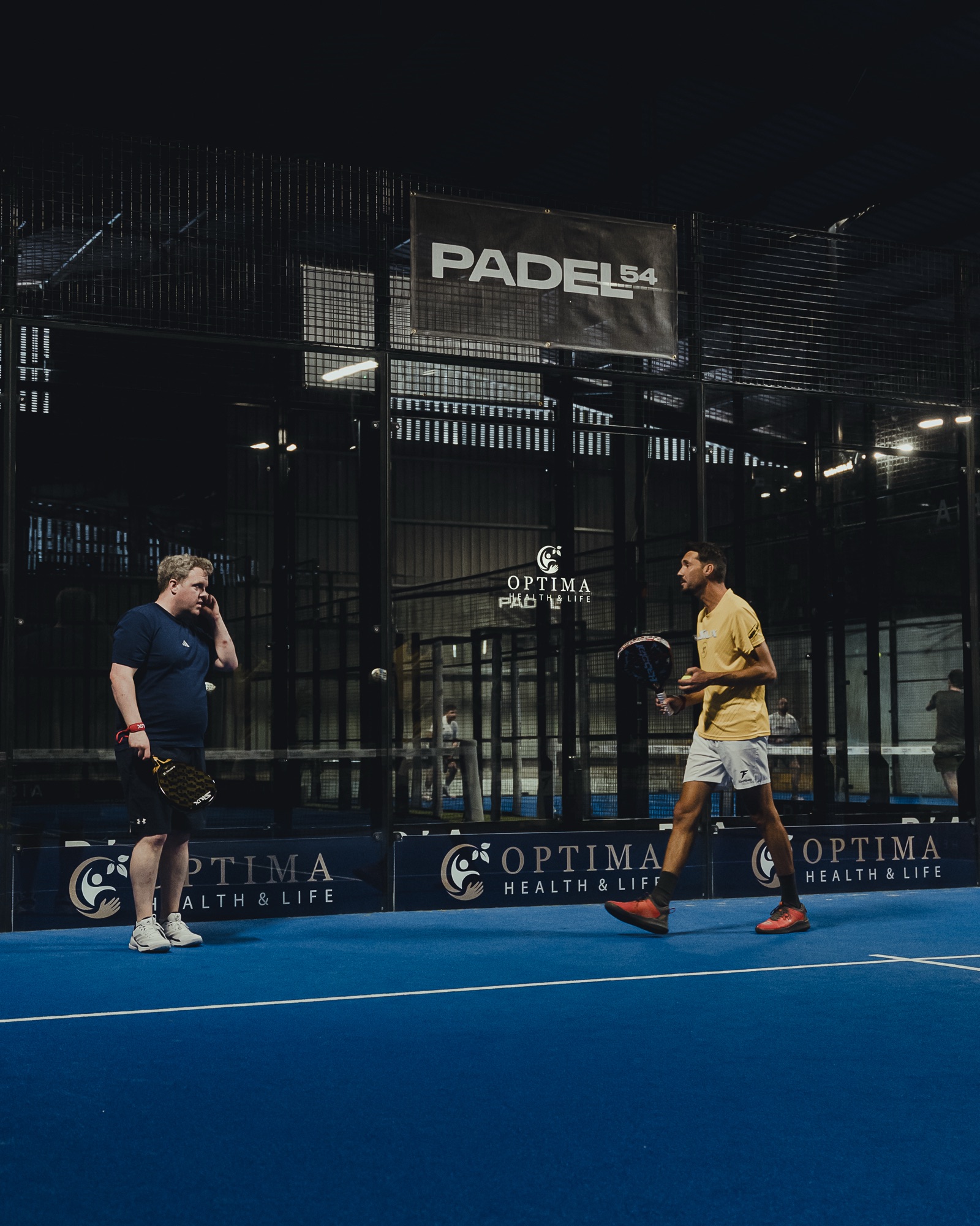 A coach talking with a player courtside at Padel54